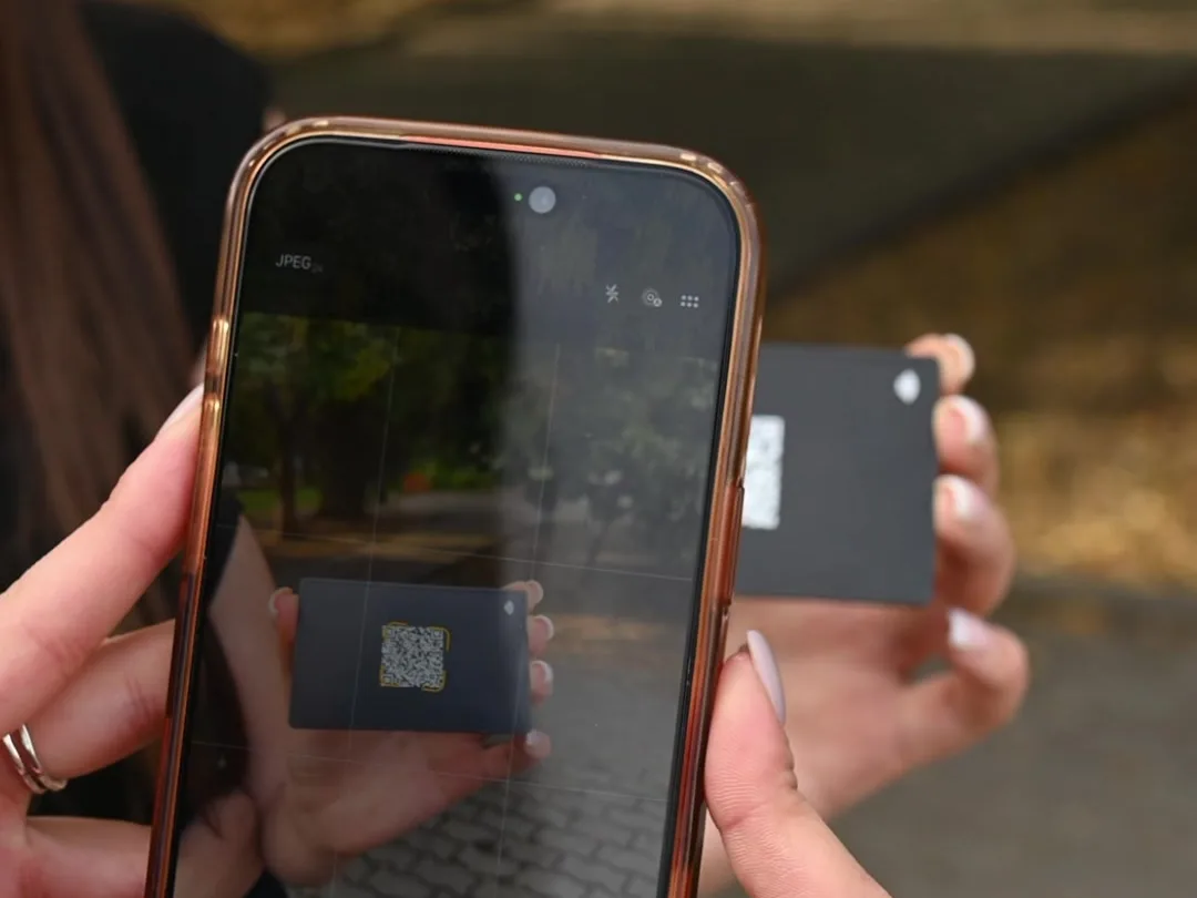 A phone camera scanning the QR code on a black Mibio metal card