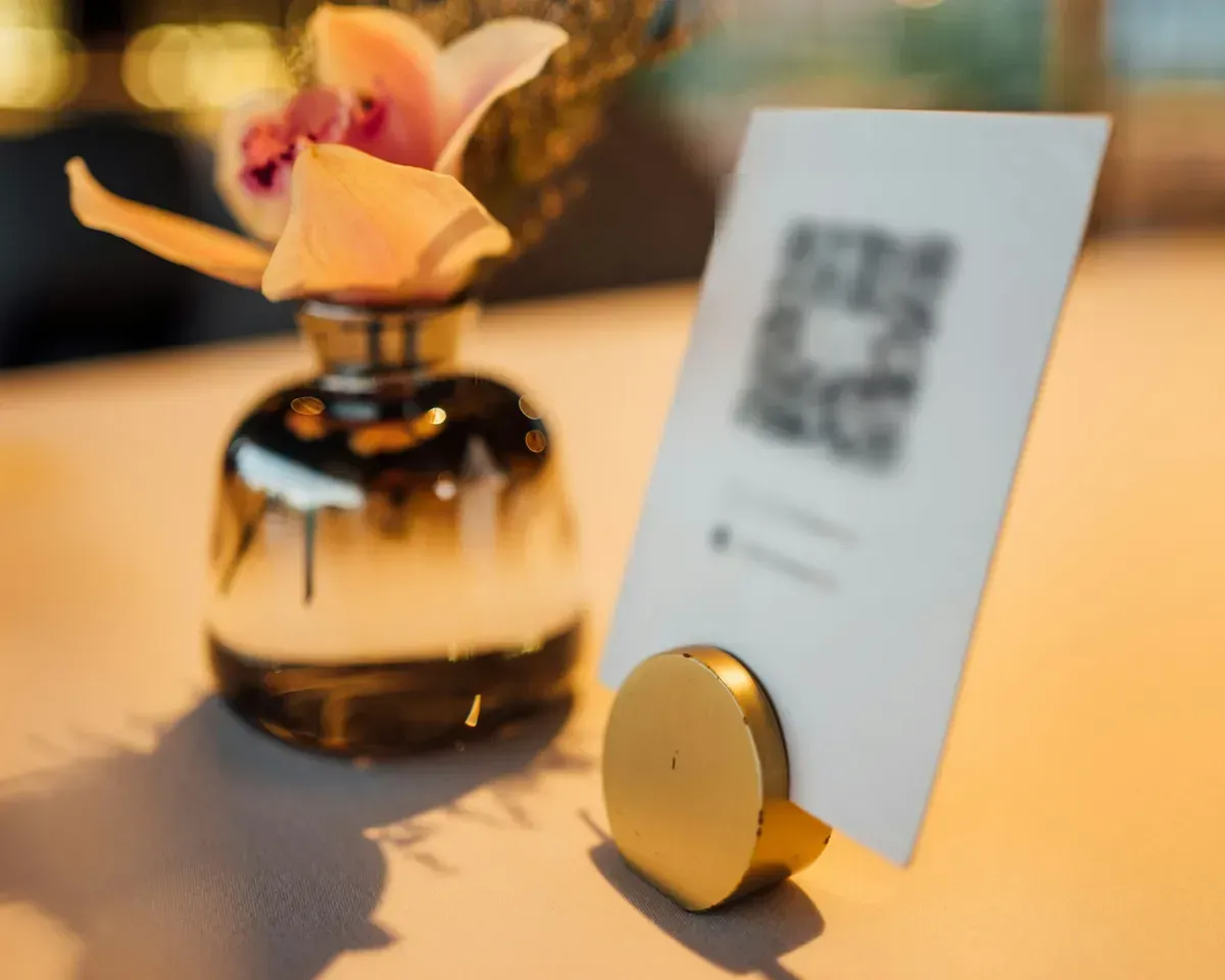 A printed QR code sign on a café table, next to a small vase