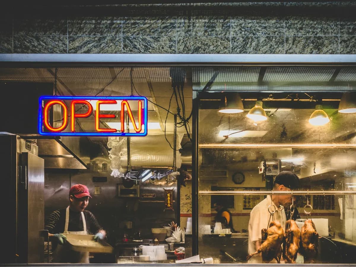 A small restaurant kitchen seen through its window, with an OPEN sign lit in neon